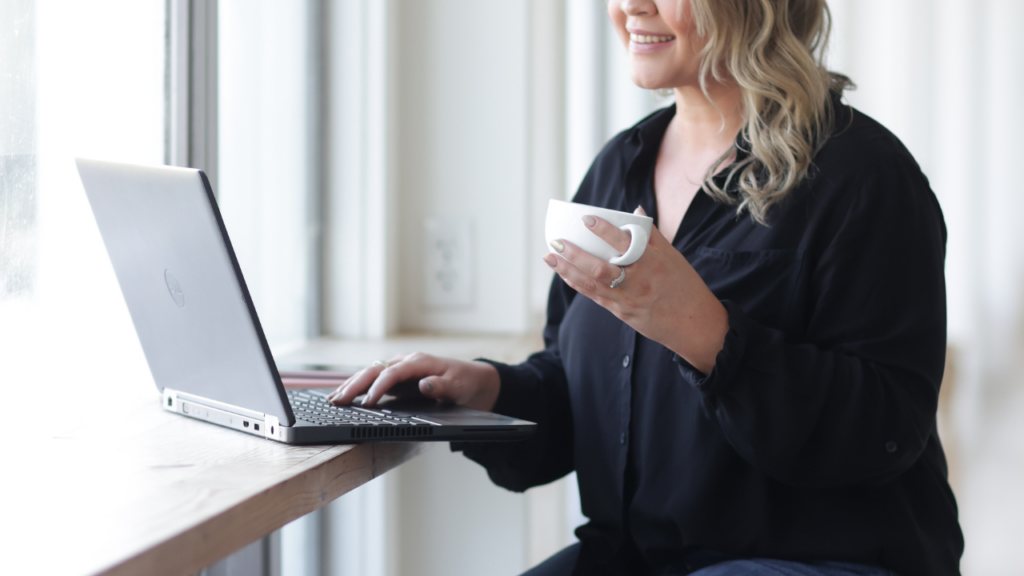 photo of woman holding a teacup while typing on her laptop