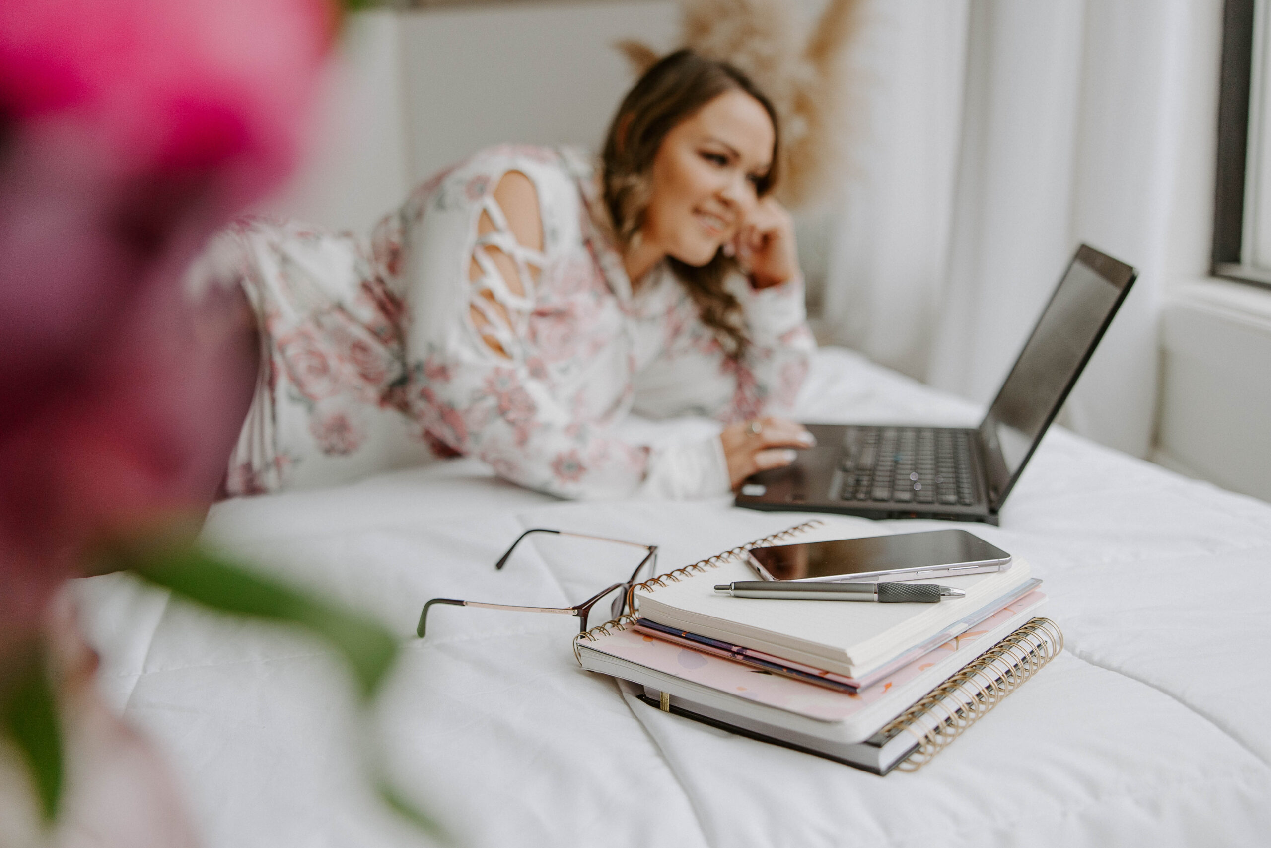 photo of woman laying on bed typing on her laptop and smiling
