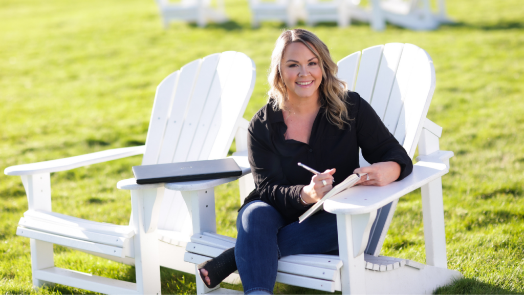 photo of woman sitting on an Adirondack chair, smiling at the camera and writing in her notebook